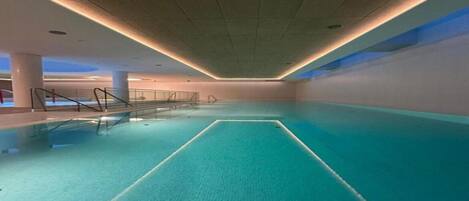 Une piscine intérieure dotée d’un sol carrelé et d’une voie centrale, entourée de murs et d’un plafond équipé d’un éclairage encastré.