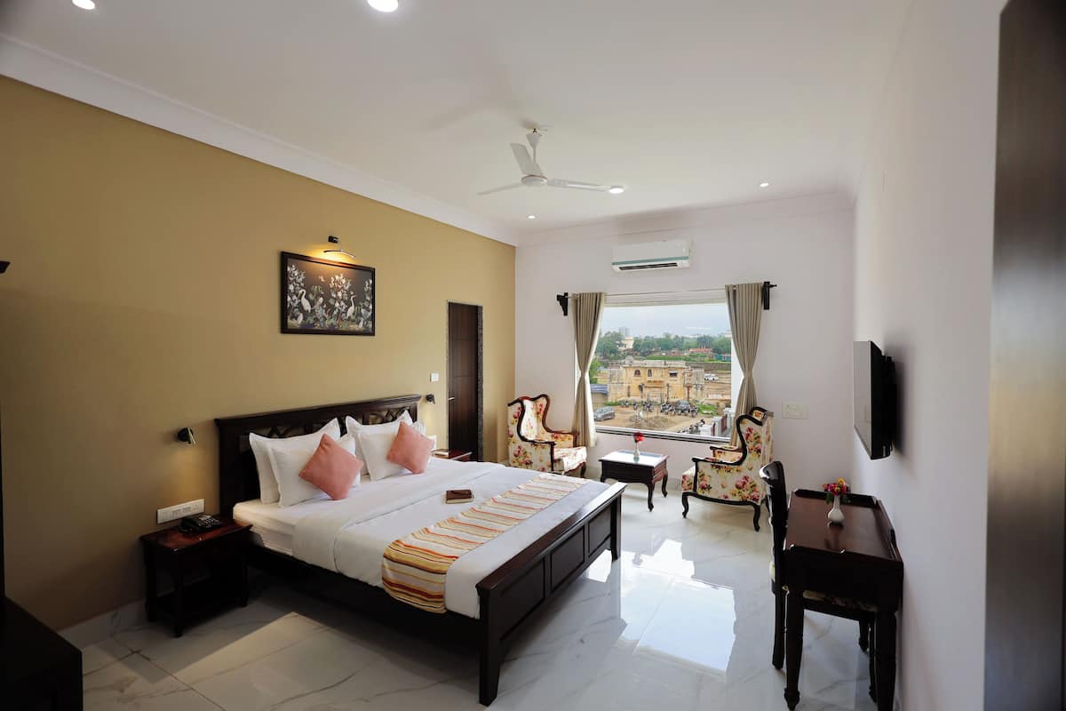 A hotel bedroom with a large bed, bedside tables, a desk, a chair, a TV, and a window with a view.