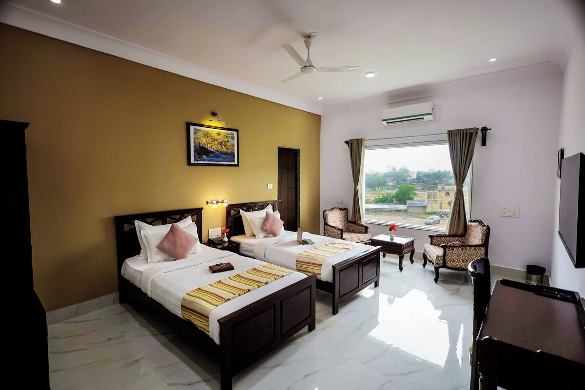 A hotel room with two beds, a desk, a chair, and a large window.