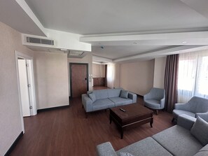 A spacious living room with a grey sofa, a matching armchair, and a wooden coffee table. - Star Suit Hotel (Trabzon)
