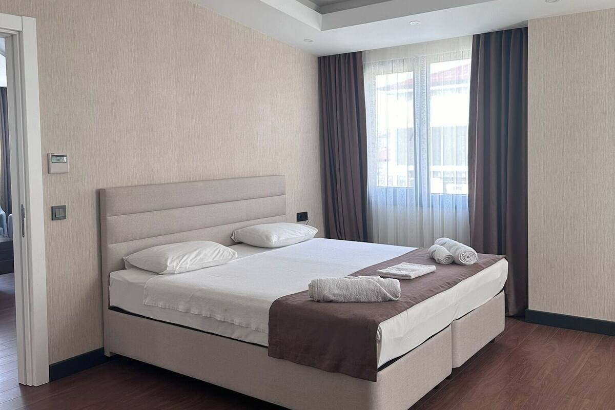 A modern hotel room with a large bed, a wooden floor, and a view of the city through the window.