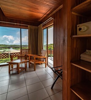 A wooden balcony with a view of a green landscape, two wooden chairs, and a shelf with towels.
