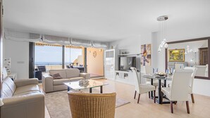A spacious living room with a glass coffee table, a sofa, and a dining area with white chairs and a glass table. - K11 Campos del Mar - Apartment (Sitio de Calahonda)