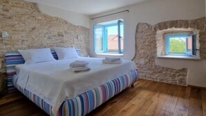 Ein Schlafzimmer mit Holzboden, einem Bett mit gestreifter Bettwäsche, einer Steinwand und einem Fenster mit Blick.