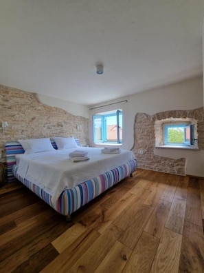 Ein Schlafzimmer mit Holzboden, einem Bett mit gestreifter Bettwäsche, einer Steinwand und einem Fenster mit Blick.