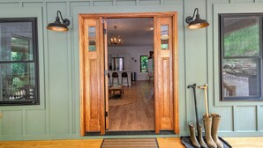A wooden door leading into a room with a dining table and chairs, a chandelier, and a window with a view of trees. - Retreat - Creek, Sliding Rock, Waterfalls, Fishing, Hiking, Hot Tub, Fire Pit (Old Fort)