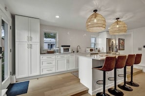 Uma cozinha moderna com armários brancos, uma ilha central com banquetas e iluminação pendente.