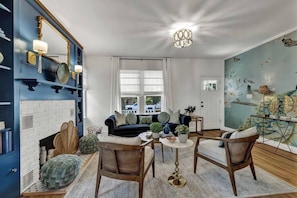 Um quarto com lareira, um sofá, uma mesa de jantar, cadeiras e um mural na parede.