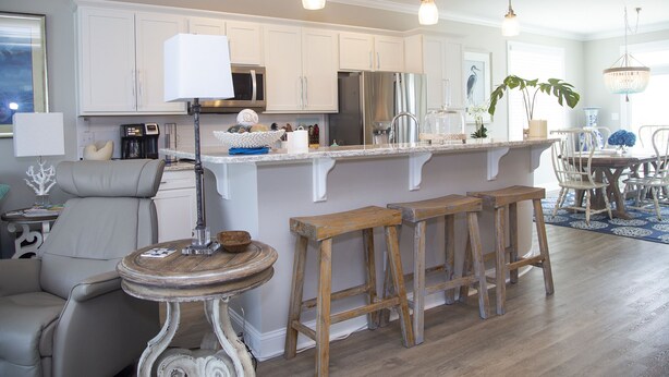 Une cuisine moderne avec des meubles blancs, un îlot central doté de tabourets, un éclairage suspendu et un coin repas avec une table et des chaises.