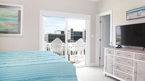 Une chambre à coucher comprenant un lit, une télévision, une commode et une porte-fenêtre coulissante donnant sur un balcon équipé de chaises.
