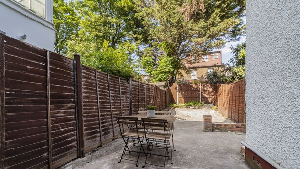 Un patio con tavolo e sedie, una recinzione in legno e un muro in mattoni.