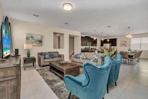 A modern living room with a sofa, coffee table, and blue armchairs. There is a TV on a wooden stand and a painting on the wall. - Pool & Spa! Solara Resort 7 mi 2 Disney! 1513 (Kissimmee)