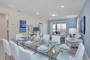 A modern dining area with a glass table, white chairs, and silver decorative items. - Pool Privacy! Fooseball! Resort 7mi 2 Disney-1220 (Davenport)