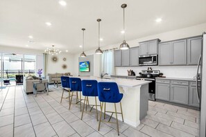 Una cocina moderna con armarios grises, una isla central con taburetes y un amplio ventanal que proporciona luz natural.