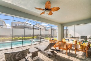 A sunlit patio with a pool, outdoor seating, and a ceiling fan.