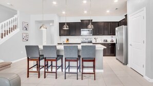 A modern kitchen with dark cabinets, a central island with bar stools, and pendant lighting. - Harry Potter | Hero Game Loft |  Pool | Disney 267 (Davenport)