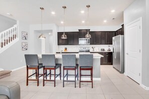 A modern kitchen with dark cabinets, a central island with bar stools, and pendant lighting. - Harry Potter | Hero Game Loft |  Pool | Disney 267 (Davenport)