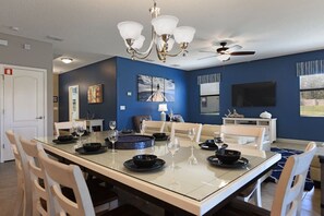 Un coin repas avec une table à plateau en verre, des chaises blanches, un lustre et un ventilateur de plafond.