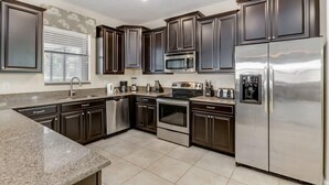 A modern kitchen with dark cabinetry, stainless steel appliances, and a granite countertop. - No Rear Neighbors | Pool & Spa | Waterpark 1447 (Davenport)