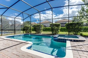 Een overdekt buitenzwembad met een jacuzzi, omgeven door een terras van baksteen en uitzicht op huizen en groen.