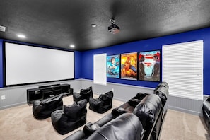 Una sala de cine en casa con una pantalla grande, varias opciones de asientos y carteles en la pared.