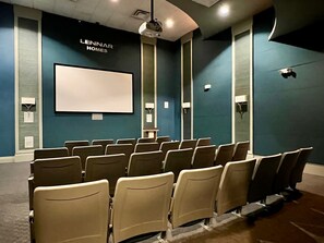 Une salle de cinéma avec des rangées de sièges beiges, un grand écran blanc et une enseigne « LENNAR HOMES » sur le mur.