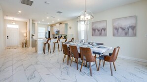 Un comedor amplio con piso de mármol, una isla central con electrodomésticos y una lámpara de cristal.