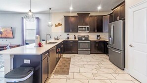 A modern kitchen with dark cabinets, stainless steel appliances, and a marble floor. - Mickey | Nemo | Theater | Gameroom | Waterpark 1521 (Four Corners)