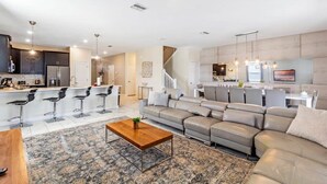 A modern living room with a large sectional sofa, a coffee table, and a kitchen area with bar stools. - Mickey | Nemo | Theater | Gameroom | Waterpark 1521 (Four Corners)