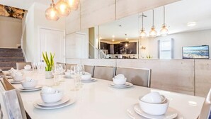 A modern dining area with a white table set for a meal, a staircase, and a kitchen in the background. - Mickey | Nemo | Theater | Gameroom | Waterpark 1521 (Four Corners)