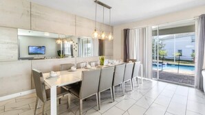 A modern dining area with a long table, chairs, and hanging pendant lights. - Mickey | Nemo | Theater | Gameroom | Waterpark 1521 (Four Corners)