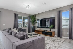 Un salon moderne avec un canapé d’angle, un téléviseur à écran plat, une table basse et une grande plante en pot.