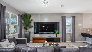 Una sala de estar moderna con un televisor de pantalla plana grande, sofás grises, una mesa de centro y una planta grande.