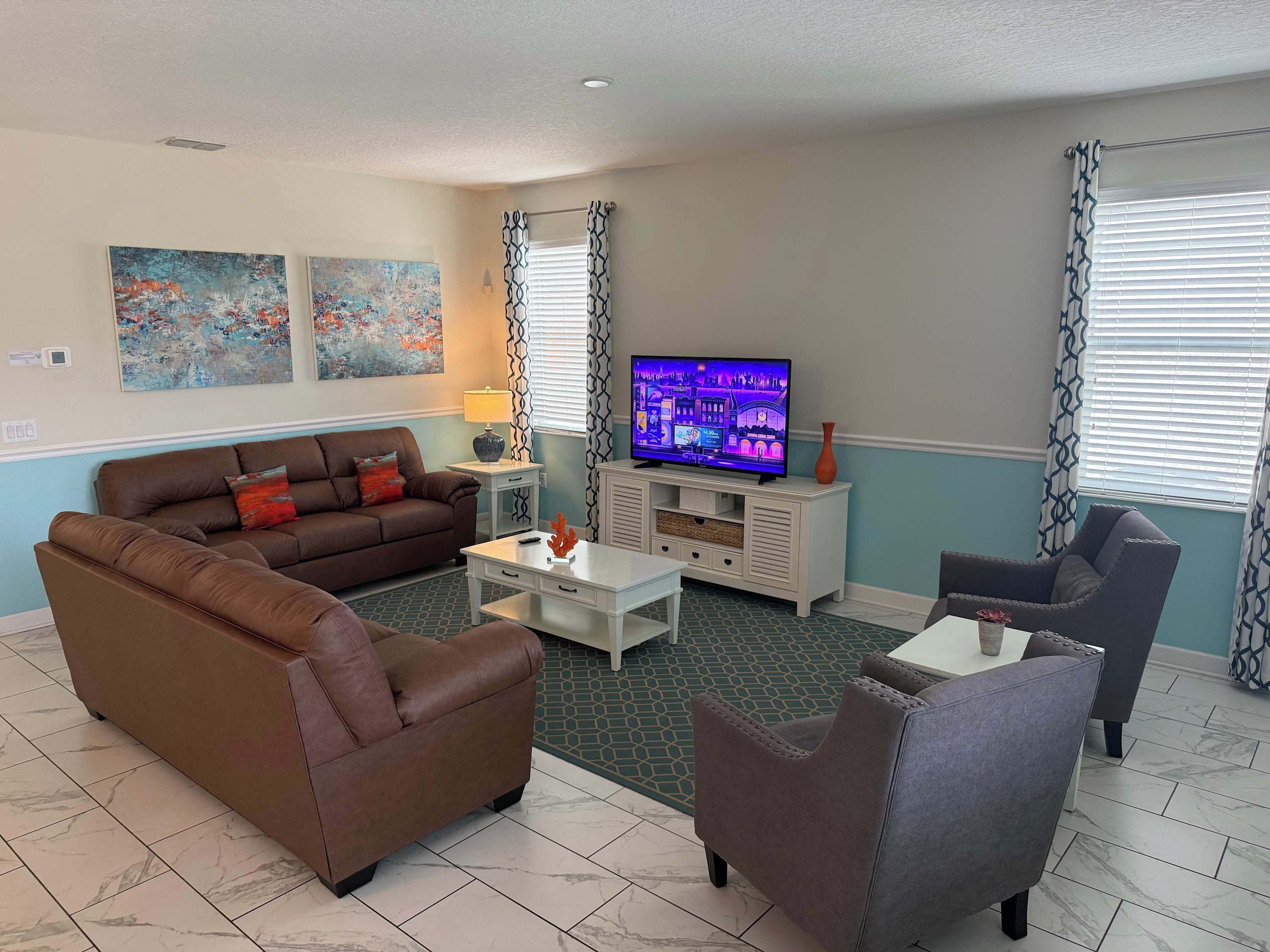 A living room with a brown sofa, a white coffee table, a grey armchair, a TV, and abstract art on the wall.