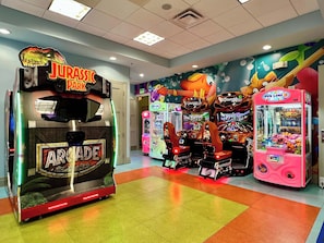 Une salle d’arcade lumineuse, dotée de différents jeux, notamment un jeu sur le thème de « Jurassic Park » et un jeu de griffe intitulé « Fun Zone ».