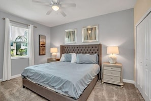 Une chambre à coucher avec un grand lit, deux tables de chevet avec des lampes, un ventilateur de plafond et des œuvres d’art accrochées aux murs.