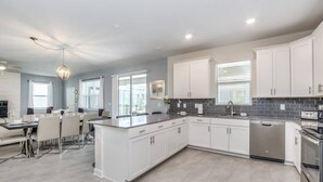 Een moderne keuken met witte kasten, een centraal eiland en een eetgedeelte met tafel en stoelen.