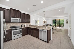 A modern kitchen with dark wood cabinets, stainless steel appliances, and a large island. - ChampionsGate | Pool & Hot Tub | Near Disney 8165 (Davenport)