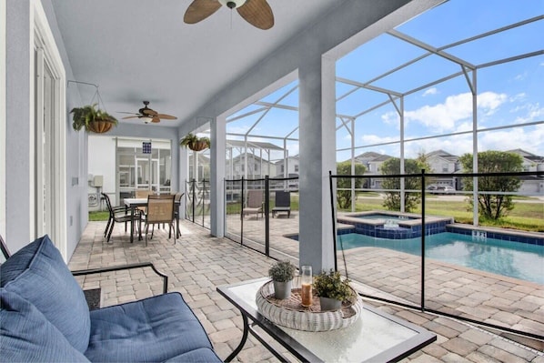 Relax on the covered patio with a sofa, dining table, and pool views.