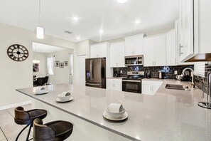 Una cocina moderna con armarios blancos, una isla central, electrodomésticos de acero inoxidable y un comedor con sillas.