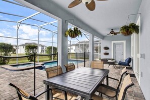 A covered patio with a pool, outdoor seating, and hanging planters.