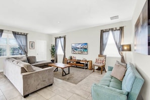 Relax in this stylish living room with a sofa set, light blue sofa, and coffee table, featuring a flat-screen TV and a floor lamp.