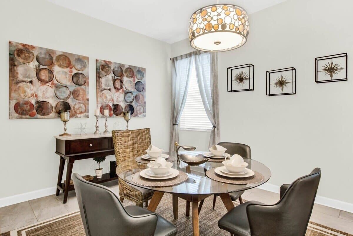 A dining area with a round table set for four, surrounded by leather chairs. There are two wall-mounted paintings above the table and three framed starburst designs on the wall.