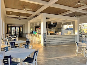 Un café en plein air avec des tables et des chaises, un comptoir avec un téléviseur et un ventilateur de plafond.