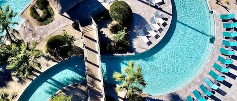 Vue aérienne d’un complexe hôtelier doté d’une grande piscine sinueuse, de chaises longues et de palmiers.