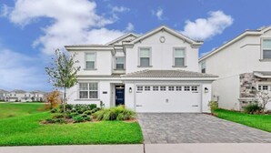 A two-story house with a garage, a well-maintained lawn, and a paved driveway. - South Pool | Gameroom | Waterpark | Near Disney 8940 (Davenport)