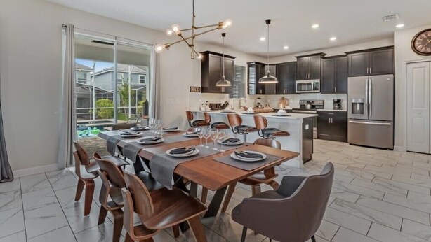 A modern kitchen with dark cabinets, stainless steel appliances, and a dining area with a wooden table and chairs. - South Pool | Gameroom | Waterpark | Near Disney 8940 (Davenport)