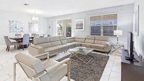 A modern living room with a sectional sofa, a glass coffee table, and a dining area with chairs and a table. - 101 Dalmatians | Theater | South Pool | Disney 8942 (Davenport)