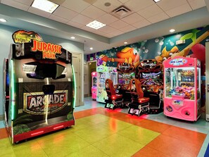 Une salle d’arcade proposant divers jeux, notamment un jeu sur le thème de « Jurassic Park » et des jeux portant la mention « Arcade ».