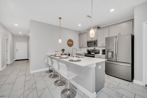 A modern kitchen with a central island, stainless steel appliances, and white bar stools.